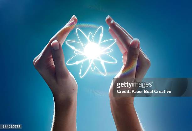 hands cupping a glowing atom in the studio - átomo imagens e fotografias de stock