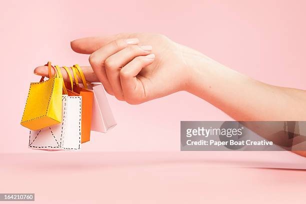 hand holding tiny shopping bags on plain pink - shopping bags stockfoto's en -beelden