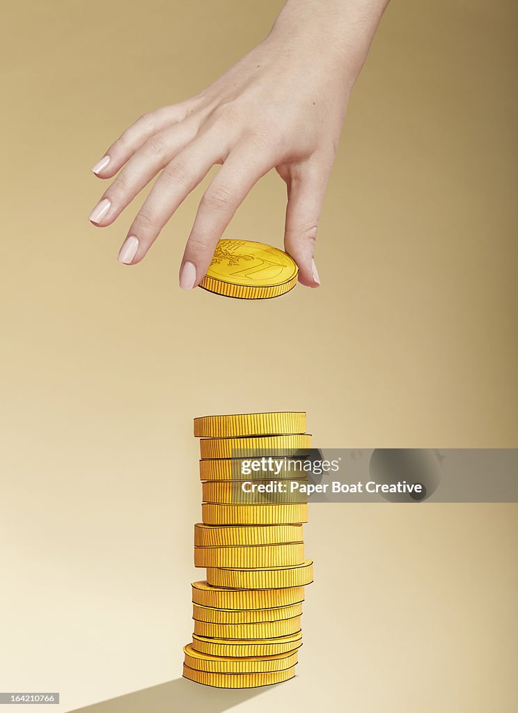 Hand putting paper gold coin on stack of coins