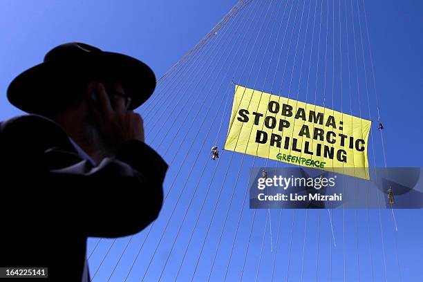 Greenpeace activists hang a banner saying 'Obama Stop Arctic drilling' on the cables of Jerusalem's Chords Bridge on March 21, 2013 in Jerusalem,...