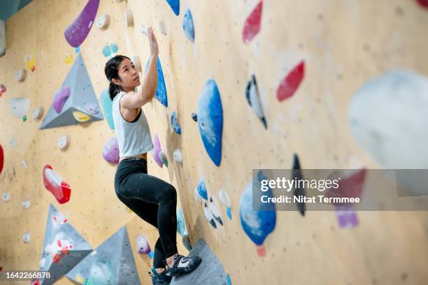 exercise can boost self-confidence and develop emotional intelligence. side view of a female climber looking up next point of a bouldering wall while climbing workout in an indoor climbing gym. - climbing wall stock pictures, royalty-free photos & images