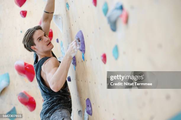 increased your muscle strength and endurance with climbing exercise. side view of a male climber climbing up on a boulder wall in an indoor rock climbing gym. - climbing wall stock pictures, royalty-free photos & images