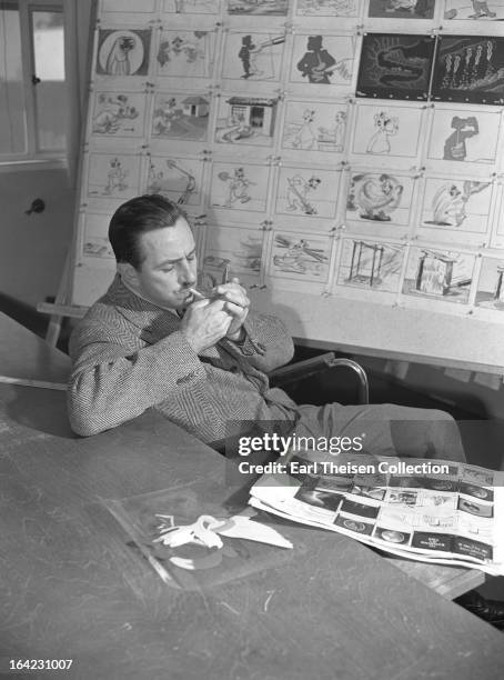 Walt Disney lights a cigarette while seated next to a storyboard for the commisioned animated short 'Hookworm' circa 1945 in Los Angeles, California.