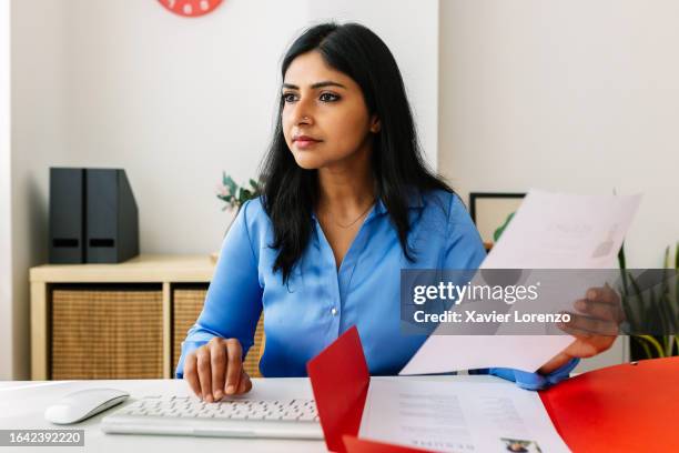 human resources indian female manager holding job applicant resume while looking at computer screen in her office. - empleada administrativa stock pictures, royalty-free photos & images