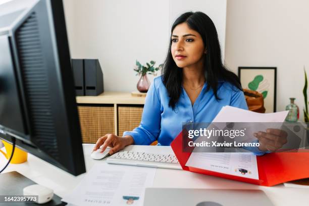 professional indian hr manager reading job candidate’s resume in her office while working on laptop. - recruiter stockfoto's en -beelden