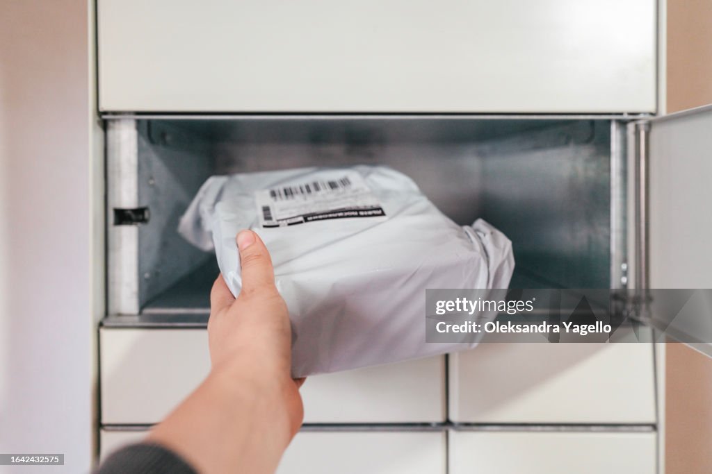 Parcel in hand on the background of a open terminal machine. Automatic parcel delivery service. Self-service storage locker.