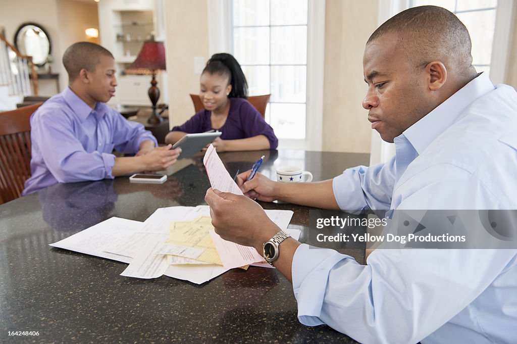 Dad paying bills, teens with digital tablet