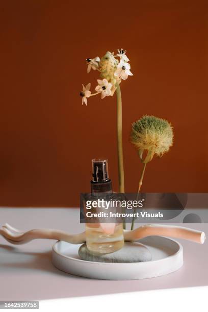 beauty product hair oil in the trasparent bottle still life composition with brown background and flowers - trasparente stock pictures, royalty-free photos & images