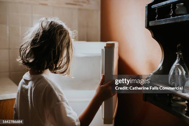 a child looks into an empty fridge-freezer in a domestic kitchen - povertà foto e immagini stock