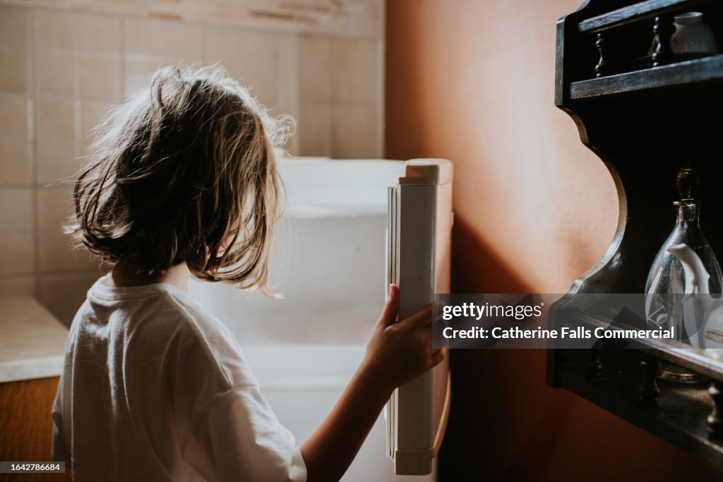 A child looks into an empty fridge-freezer in a domestic kitchen