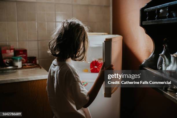 a child looks into an empty fridge-freezer in a domestic kitchen - frigo vuoto foto e immagini stock