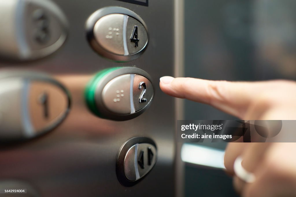 A finger pressing an elevator button, identified with numbers, gray buttons with black numbers.