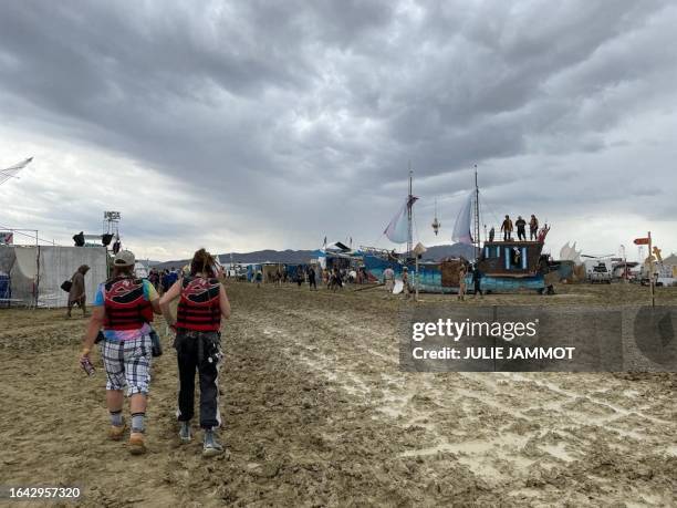 Attendees walk through a muddy desert plain on September 2 after heavy rains turned the annual Burning Man festival site in Nevada's Black Rock...