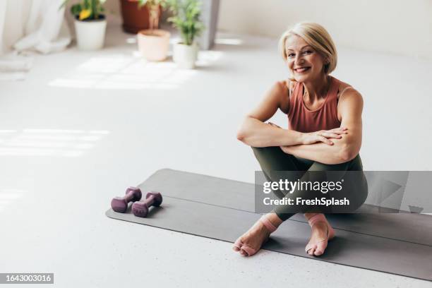 a happy blonde senior woman looking at camera after doing yoga at home - mature women stock pictures, royalty-free photos & images