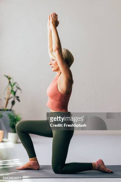 a blonde senior woman doing her daily workout while standing on yoga mat - mature woman beauty arm stockfoto's en -beelden