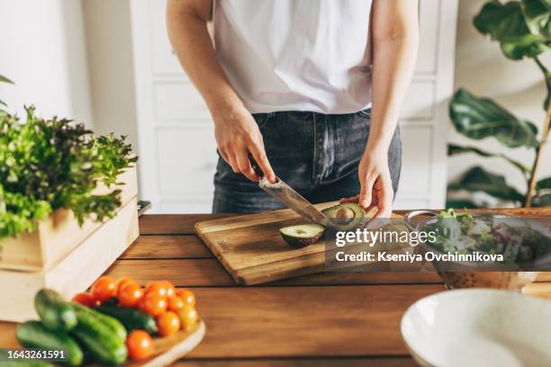 close up of woman slicing avocado on wooden board at home. vegetarian food concept - cutting avocado stockfoto's en -beelden