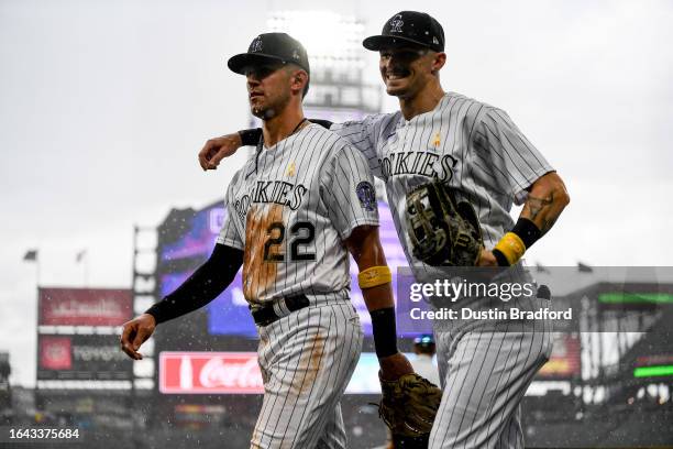 Brenton Doyle of the Colorado Rockies puts his arm around teammate Nolan Jones as they return to the dugout as a rain delay is called as heavy rain...