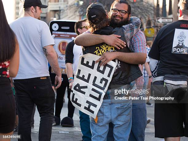 Man holding a "free hugs" sign embraces a stranger on 6th Street in Austin, Texas during SXSW 2013