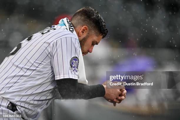 Austin Wynns of the Colorado Rockies looks on from the dugout as rain falls in the ninth inning of a game against the Toronto Blue Jays at Coors...