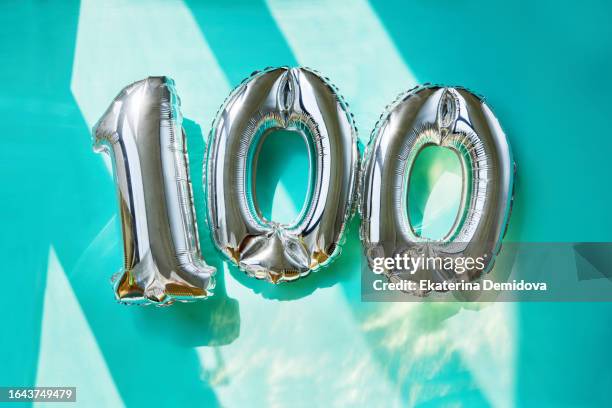 silver numbers 100 one hundred years balloons in sunlight turquoise background - centième anniversaire photos et images de collection