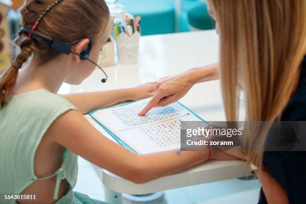 niña con auriculares y lectura asistida por un especialista en terapia del habla - tecnología de asistencia fotografías e imágenes de stock