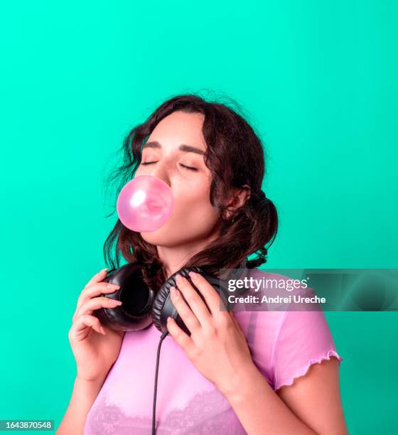 woman blowing bubble gum and listening to music with headphones, isolated on a green background - headphones isolated ストックフォトと画像