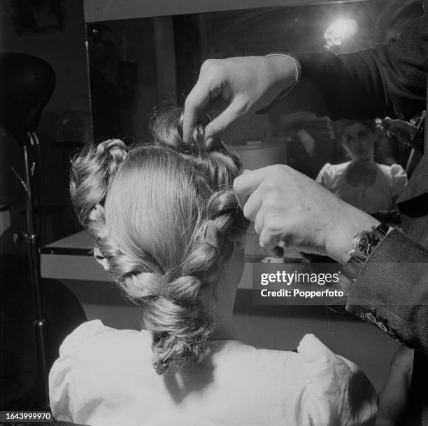 Hairdresser and hair stylist at work securing a velvet threaded plait to give length to a pony tail hair style of a female client at Raymond...