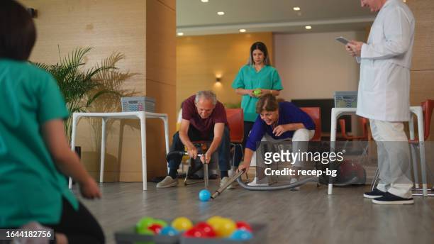 senior men and senior women trying to catch balls with vacuum cleaner as part of physical therapy session in nursing home - vacuum cleaner woman stockfoto's en -beelden