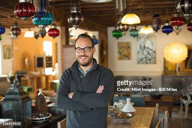 a man standing in a shop full of antique and decorative objects. antique shop displays. lighting, glass shades and furniture.  - man in antique shop stock pictures, royalty-free photos & images