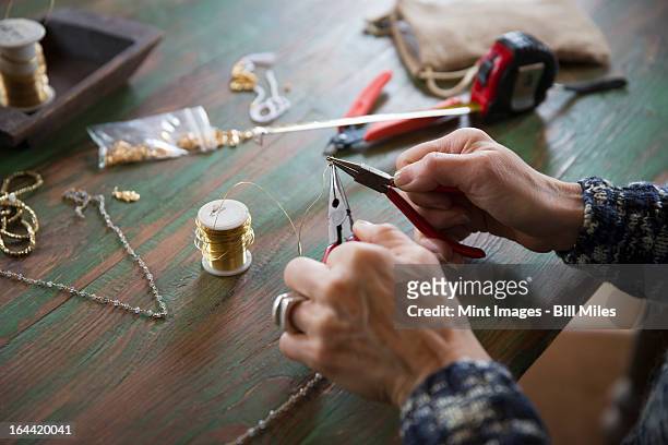 a tabletop with jewellery making equipment. hands twisting wire on a necklace. - bead string stock pictures, royalty-free photos & images
