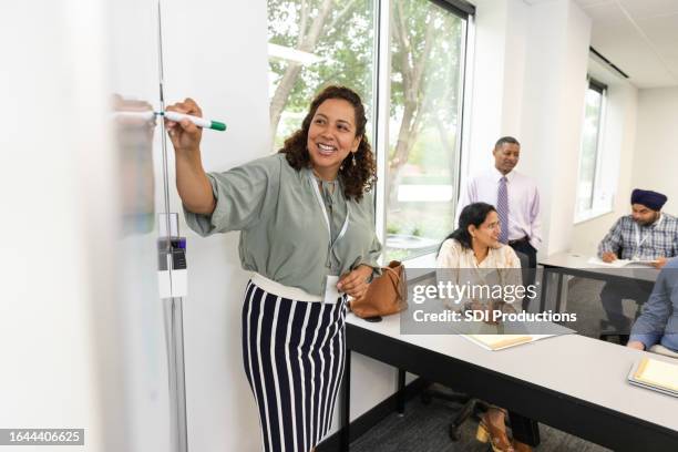 alors que les étudiants adultes réfléchissent à des idées, une professeure écrit sur un tableau blanc - réunion du personnel photos et images de collection