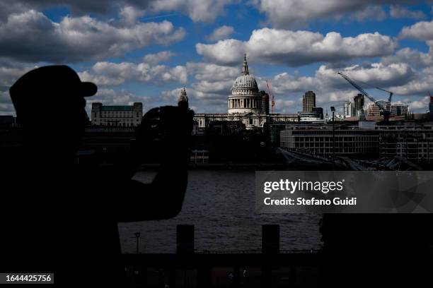 Man takes a photo with smartphone of St. Paul's Cathedral and Millennium Bridge seen from a panoramic balcony of the Tate Modern Museum on August 21,...