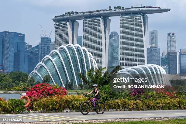 Woman rides her bicycle with the Marina Bay Sands hotel and high rise buildings in the background in Singapore on September 4, 2023.