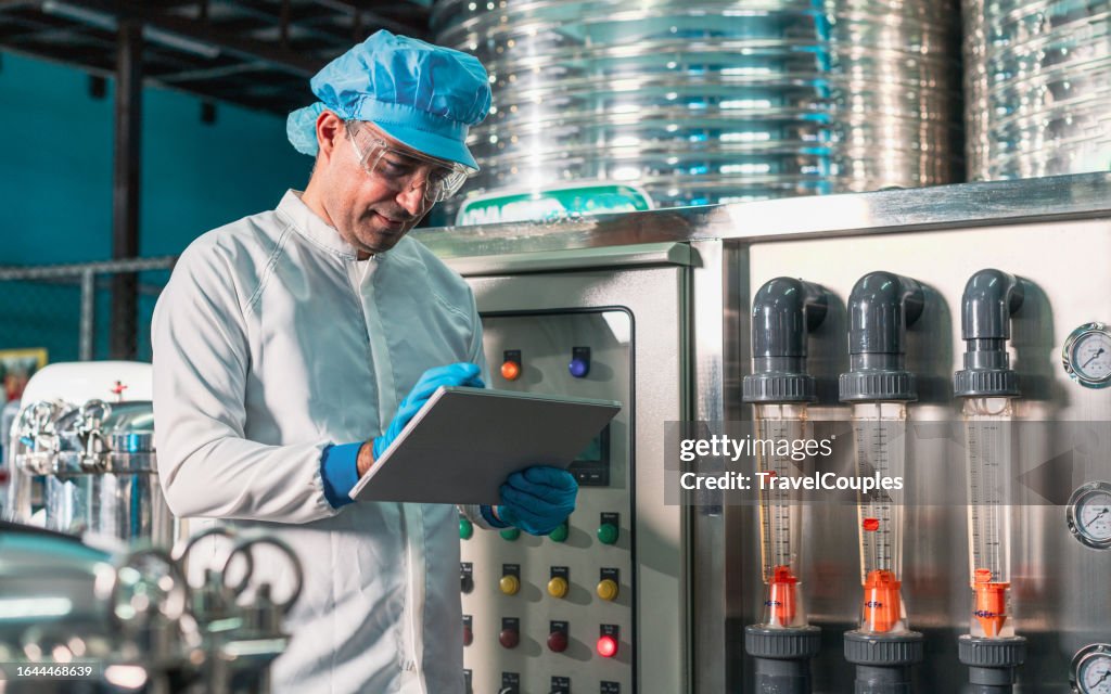 Male worker using digital tablet checking quality drinking water management system before process of filling water into bottles to bring out to consumers. Water production line of factory.