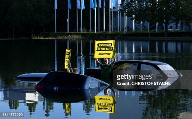 Greenpeace activists stand in a pond with old cars and hold placards near the entrance of the International Motor Show held in Munich, southern...