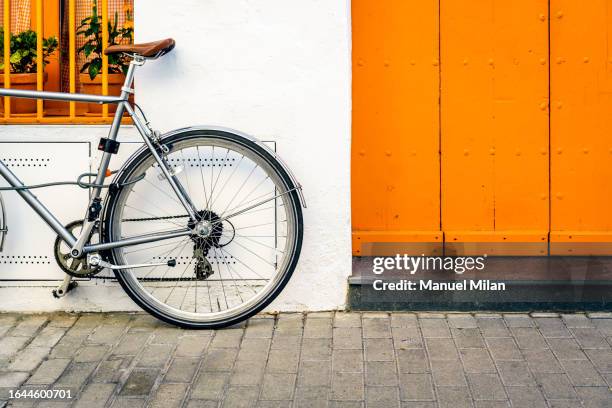 Facade of a white house with a barred window and flower pots inside and a parked bicycle.