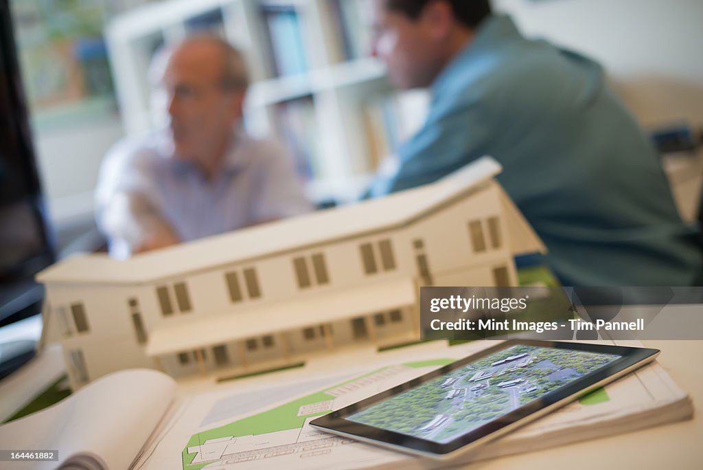 Architects working on a green construction project, using computer technology, in an office. An architect's model of a house. Computer tablet. 
