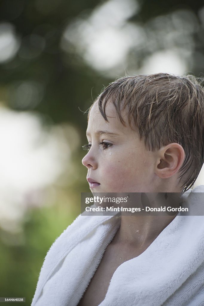 A young boy with wet hair, wrapped in a towel after swimming.