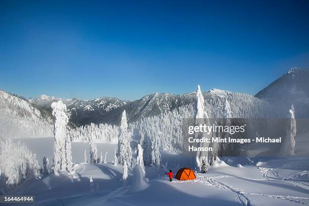 a man walking through deep powder to his campsite in the snow covered cascade mountains overlooking snow lake. - seattle winter stock pictures, royalty-free photos & images