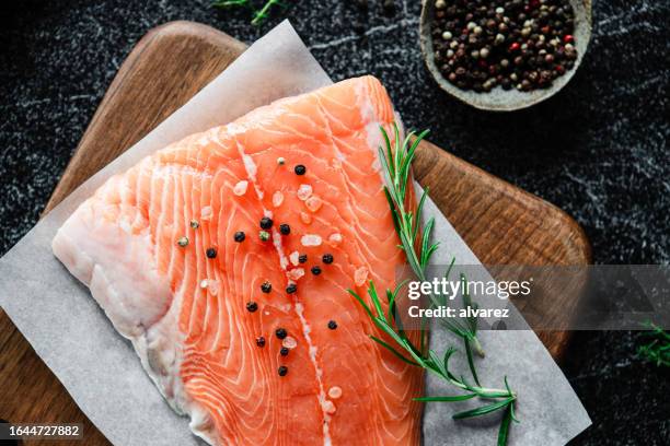top view of raw salmon steak with rosemary and black pepper on black table - fillet stock pictures, royalty-free photos & images