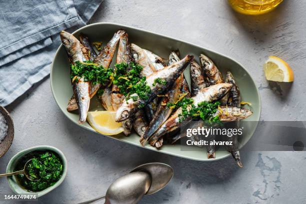 hausgemachter gegrillter fisch mit knoblauch, frischer petersilie und zitrone auf einem teller serviert - fischfutter stock-fotos und bilder