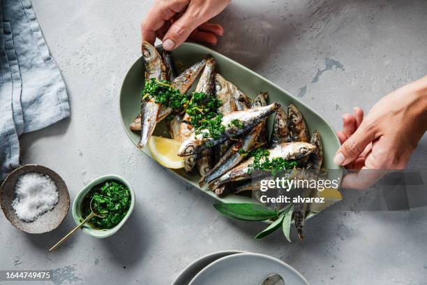 manos de mujer sirviendo sardinas a la parrilla con especias en una mesa - preparación de alimentos fotografías e imágenes de stock
