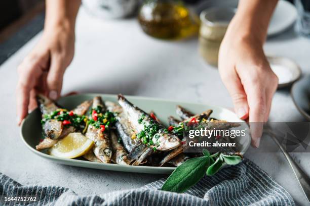 woman's hand serving fried fish with lemon on dining table - sardinha imagens e fotografias de stock