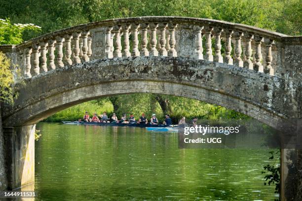 Rowing on the Thames at Iffley, seen through the arch of a stone bridge.