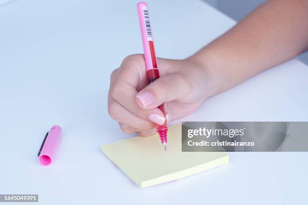 girl writing with pink pen on adhesive notes - cristinairanzo stock pictures, royalty-free photos & images