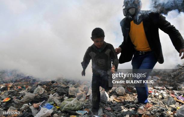 Syrian man escorts a boy away from fumes as a street covered with uncollected garbage is fumigated in the northern city of Aleppo on March 24, 2013....