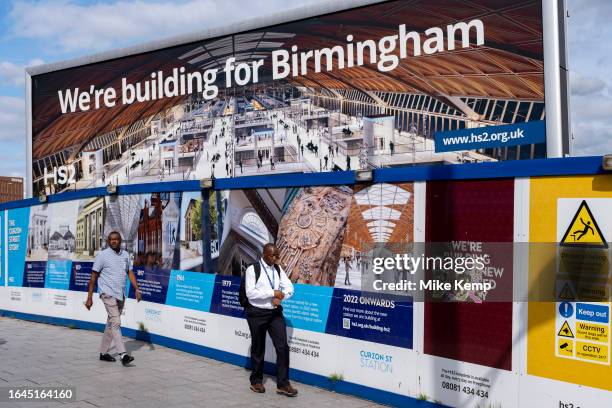People pass a large scale billboard advertising poster as work continues at the construction site for the HS2 mainline station at Curzon Street on...