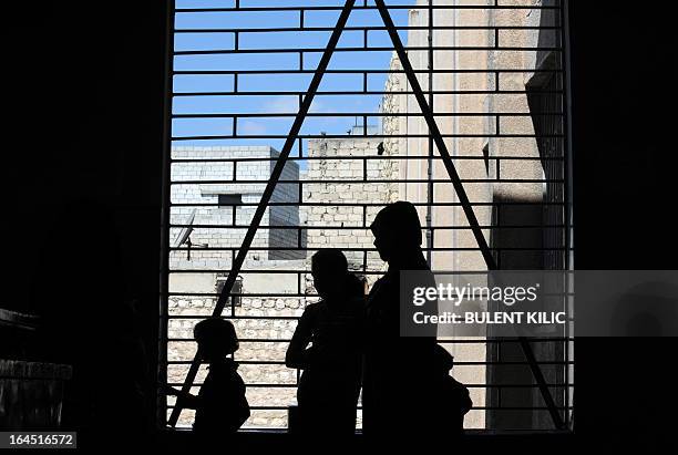 Syrian woman and her children are seen in silhouette as they look out a window in the northern city of Aleppo on March 24, 2013. Syria's mainstream...