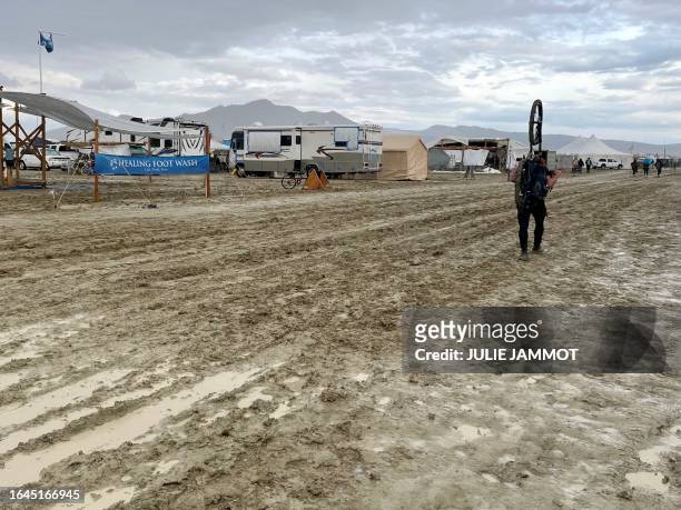 Attendees walk through a muddy desert plain on September 3 after heavy rains turned the annual Burning Man festival site in Nevada's Black Rock...