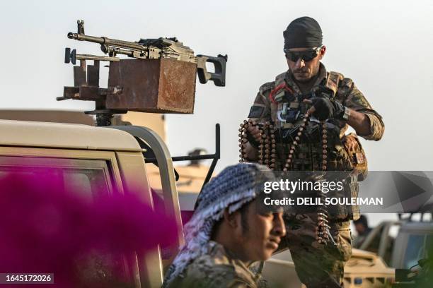 Fighter of the Syrian Democratic Forces loads a machine gun belt onto a turret along a technical vehicle as others deploy to impose a curfew in the...